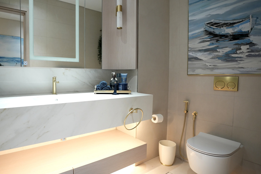 Beach Walk Residence A modern bathroom featuring a sleek vanity with mirror, gold fixtures, and a boat painting on the wall.